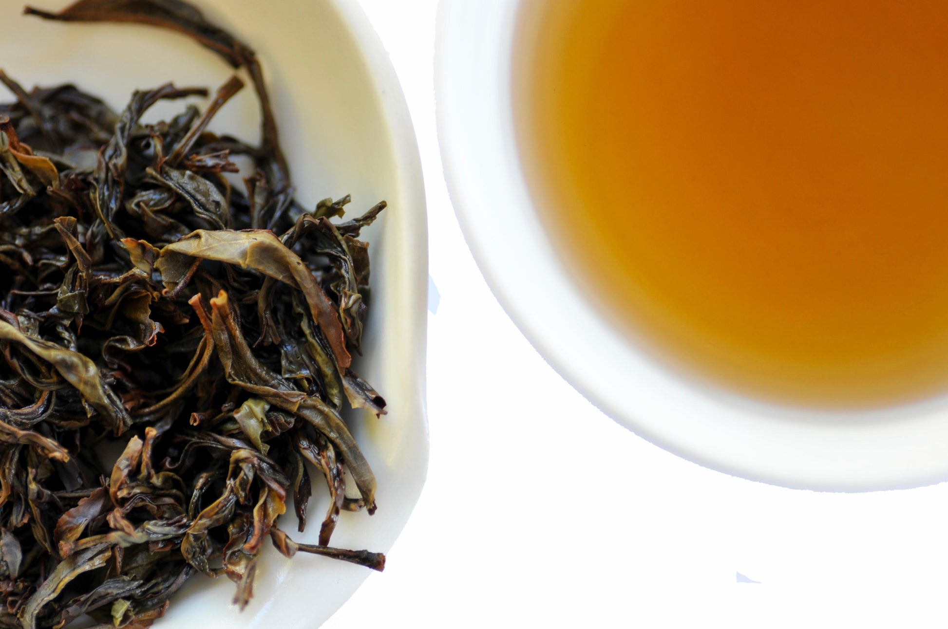 Wet tea leaves on one side and a cup of brewed tea on the other, on a white background.