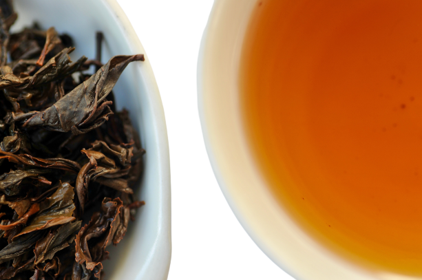 Close-up of tea leaves and a cup of tea on a white background